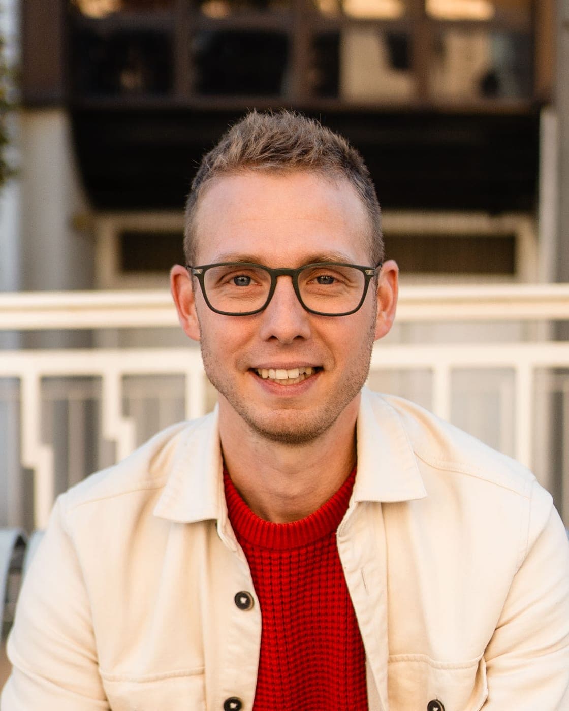 Portrait de Guillaume Maurice, souriant, de face, en veste claire et pull rouge
