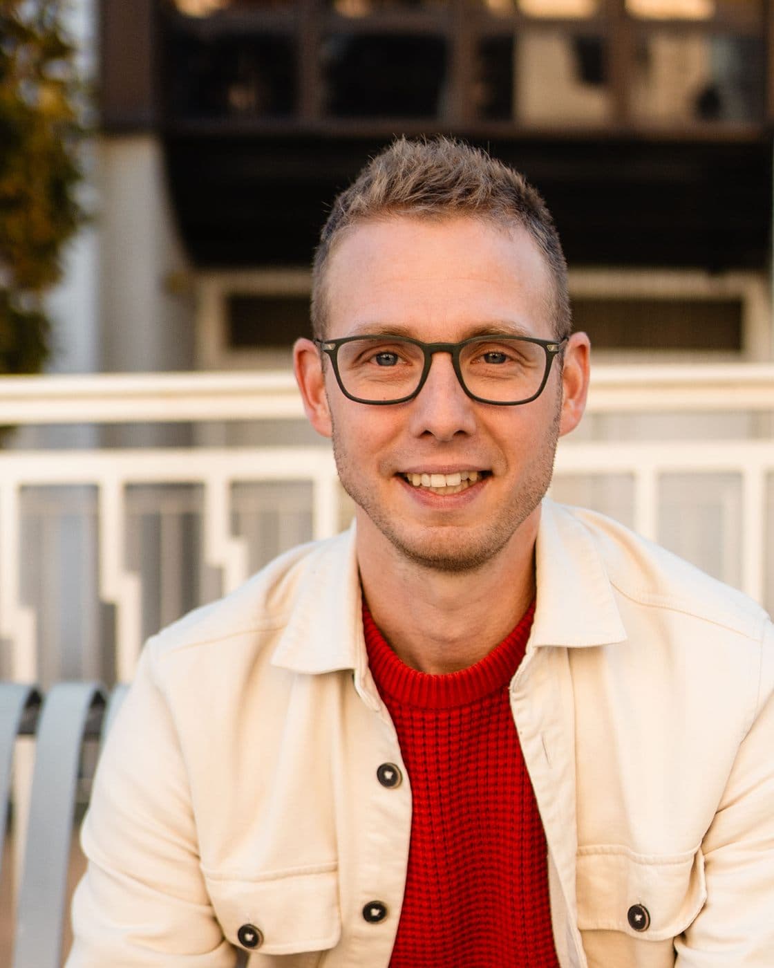 Portrait de Guillaume Maurice, souriant, de face, en veste claire et pull rouge